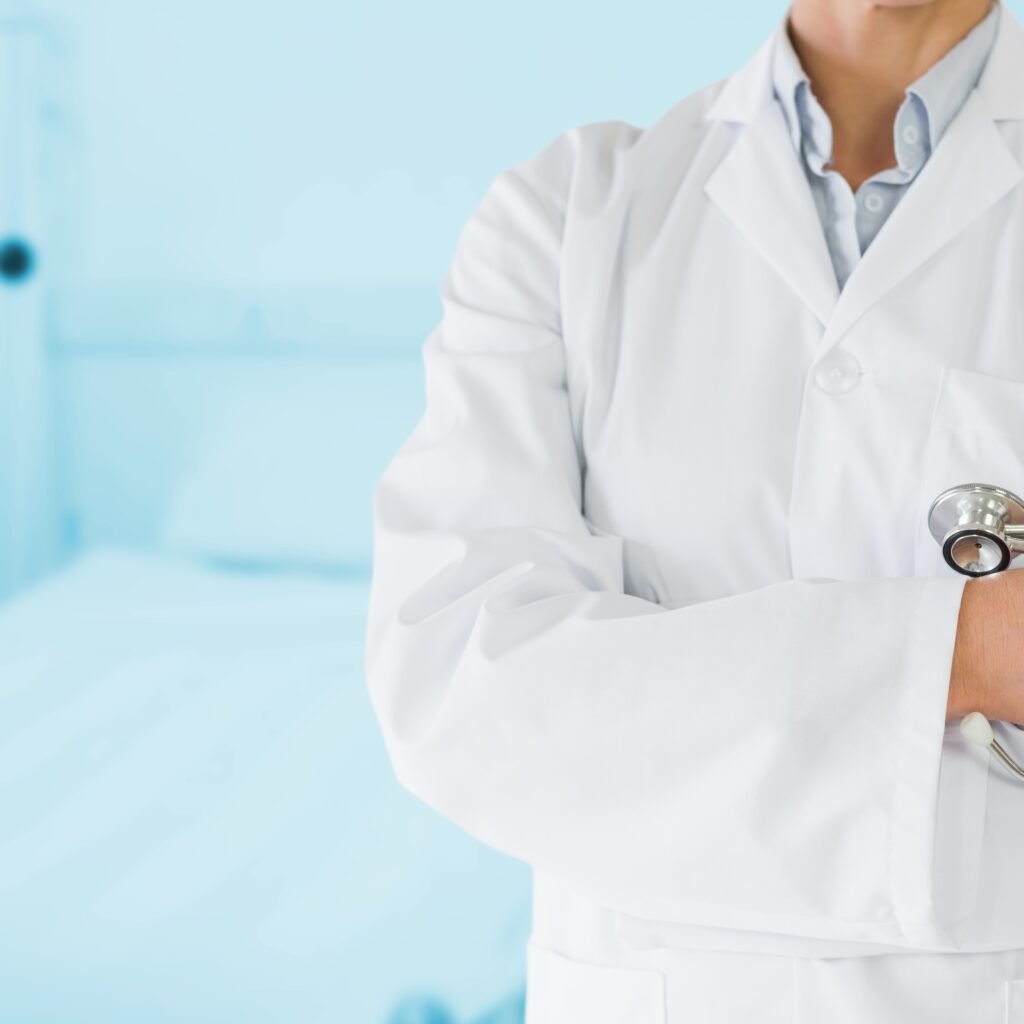 Mid section of doctor wearing laboratory coat and holding stethoscope in hospital